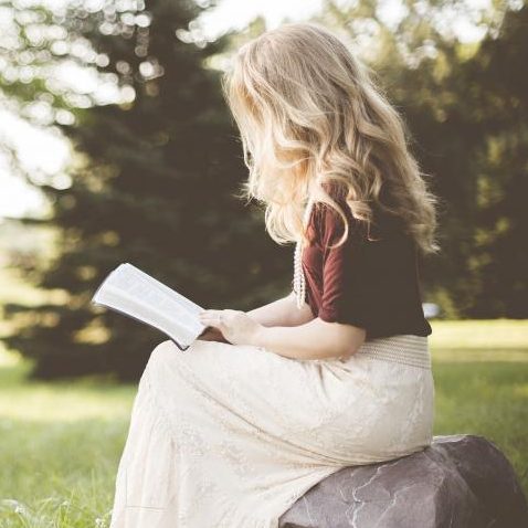 Hypnotherapy for personal growth Rebecca sitting on a rock, reading a book in a park with lush greenery.